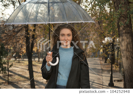 Portrait of cute woman with long hair under transparent umbrella. Beautiful girl stands on alley of fall park 104252948