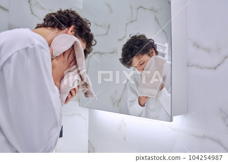 Young guy in bathroom near mirror washing face, wiping with towel 104254987