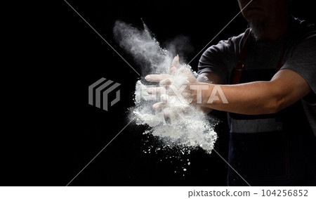 Chef prepare white flour dust for cooking bakery food. Elderly man Chef clap hand, white flour dust explode fly in air. Flour stop motion in air with freeze high speed shutter, black background 104256852