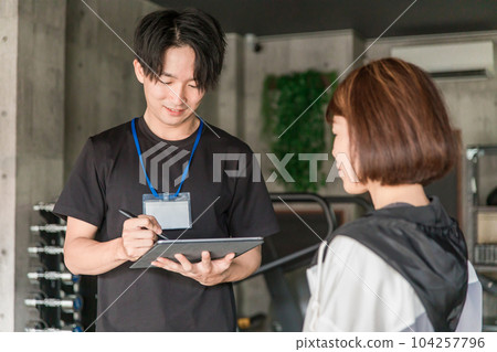 A man of a personal trainer instructor who consults counseling and exercise menu at the gym A man of a personal trainer instructor who consults counseling and exercise menu at the gym 104257796