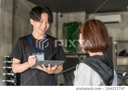 A man of a personal trainer instructor who consults counseling and exercise menu at the gym 104257797