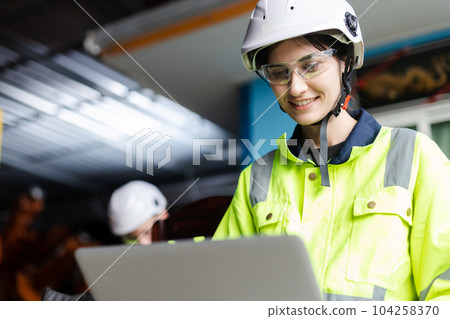 female technician engineer using laptop checking automation robotics at industrial modern factory. 104258370