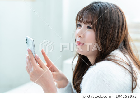 A young woman lying down and using a smartphone A young woman lying down and using a smartphone 104258952