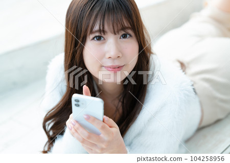 A young woman lying down and using a smartphone A young woman lying down and using a smartphone 104258956