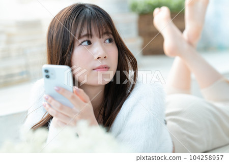 一名躺下並使用智能手機的年輕女子 104258957