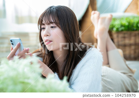 一名躺下並使用智能手機的年輕女子 104258970