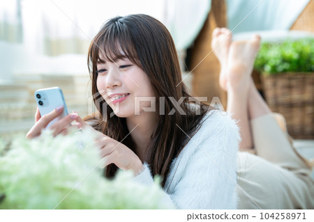A young woman lying down and using a smartphone A young woman lying down and using a smartphone 104258971