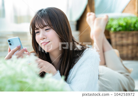 A young woman lying down and using a smartphone A young woman lying down and using a smartphone 104258972