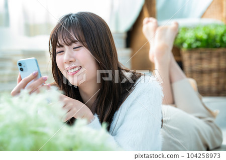 A young woman lying down and using a smartphone A young woman lying down and using a smartphone 104258973