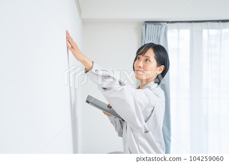 A woman in work clothes checking the condition of a house wall A woman in work clothes checking the condition of a house wall 104259060