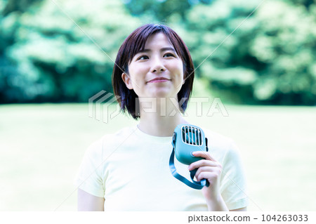 A woman cooling off with a portable fan in a fresh green park 104263033