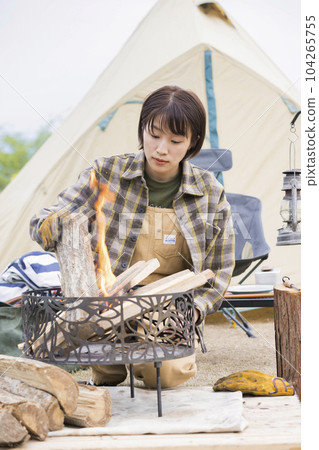 A young woman who grows a fire by adding firewood while watching the fire, bonfire, outdoor solo camp A young woman who grows a fire by adding firewood while watching the fire, bonfire, outdoor solo camp 104265755