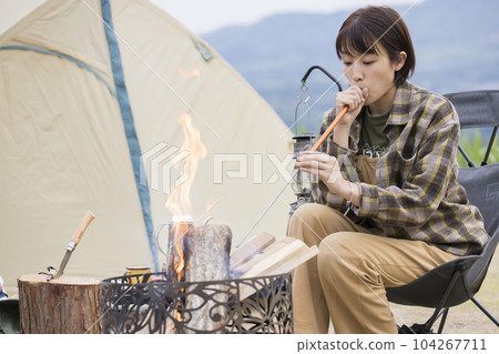 A young woman blowing air into a bonfire using a fire blowing stick, bonfire, outdoor solo camp A young woman blowing air into a bonfire using a fire blowing stick, bonfire, outdoor solo camp 104267711
