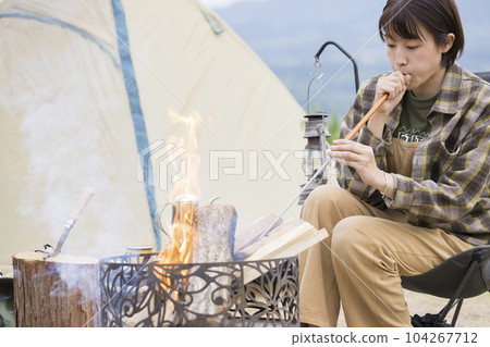 一位年輕女子用吹火棒、篝火、戶外單人營地向篝火吹空氣 104267712
