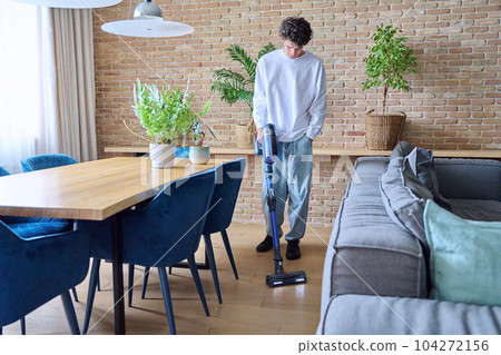 Young guy doing vacuuming, at home in the living room 104272156