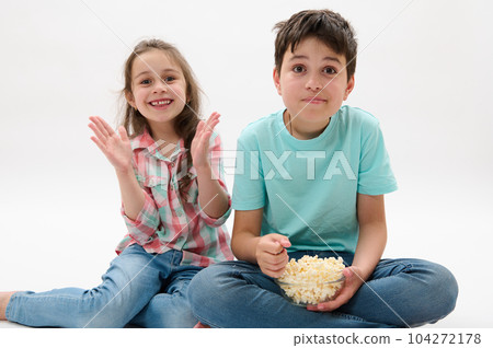 Portrait on white background of beautiful kids, teenager boy and preschooler girl, older brother and younger sister eating popcorn, expressing happy positive emotions, isolated on white background 104272178