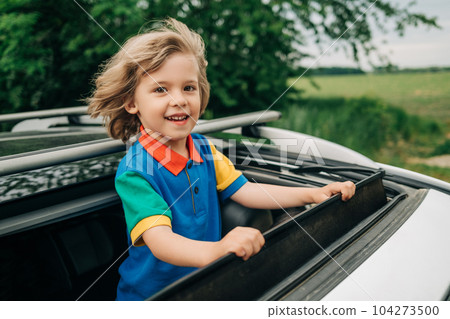Adorable happy little boy stands in open car sunroof during trip at summer. 104273500