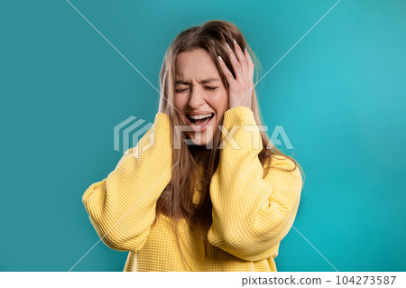Woman afraid of something, she in shock on blue backdrop.Holding head, screaming Woman afraid of something, she in shock on blue backdrop.Holding head, screaming 104273587