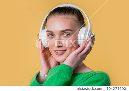 Positive teenager girl listening music, enjoying headphones on yellow background 104273600