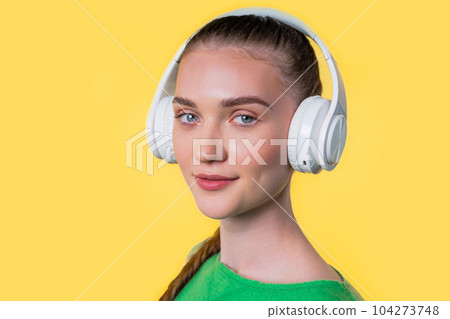 Positive teenager girl listening music, enjoying headphones on yellow background Positive teenager girl listening music, enjoying headphones on yellow background 104273748