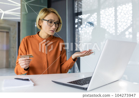 Sad and unhappy woman inside workplace office with laptop holding bank credit card, businesswoman cheated got negative account balance and online money transfer error. Sad and unhappy woman inside workplace office with laptop holding bank credit card, businesswoman cheated got negative account balance and online money transfer error. 104273947