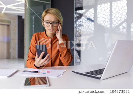 Sad upset woman pensive with phone in hands working inside office at workplace, businesswoman financier received notification message with bad news online, uses app on smartphone. Sad upset woman pensive with phone in hands working inside office at workplace, businesswoman financier received notification message with bad news online, uses app on smartphone. 104273951