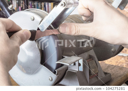 Knife sharpener and hand with blade on table, closeup 104275281