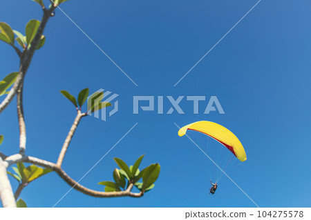 Yellow paraglider in the blue sky. The sportsman flying on a paraglider. Yellow paraglider in the blue sky. The sportsman flying on a paraglider. 104275578