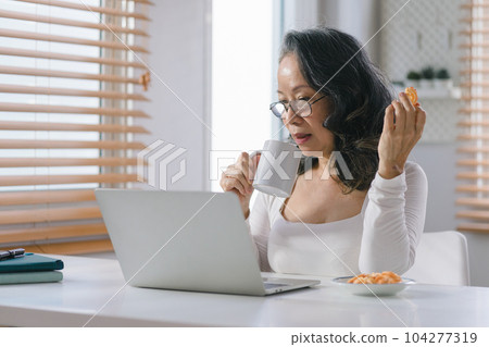 Portrait of a Senior businesswoman remote working from home distance office on smartphone taking notes. Smiling 60s middle aged business lady using smartphone watching webinar and writing in notebook. 104277319