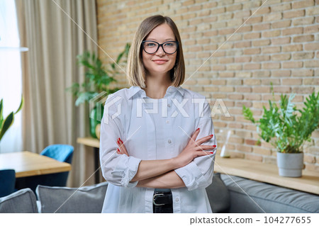 Portrait of young positive woman with arms crossed, in living room Portrait of young positive woman with arms crossed, in living room 104277655