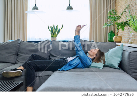 Young woman having video call lying on sofa at home, using smartphone Young woman having video call lying on sofa at home, using smartphone 104277656