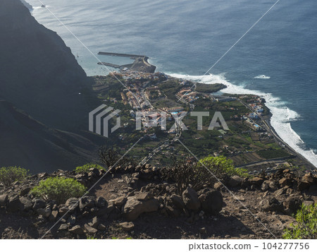 Aerial view of village resort Vueltas with port, Seen from top of La Merica mountain cliffs, Camino La Merica hiking trail. Valle Gran Rey, La Gomera, Canary Islands. Copy space. Aerial view of village resort Vueltas with port, Seen from top of La Merica mountain cliffs, Camino La Merica hiking trail. Valle Gran Rey, La Gomera, Canary Islands. Copy space. 104277756