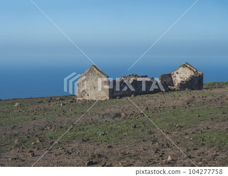 Abandoned ruins of farm house at flat plateau on top of La Merica mountain with cacti, stones and sea view. valle Gran Rey, La Gomera, Canary Islands. Copy space. Abandoned ruins of farm house at flat plateau on top of La Merica mountain with cacti, stones and sea view. valle Gran Rey, La Gomera, Canary Islands. Copy space. 104277758