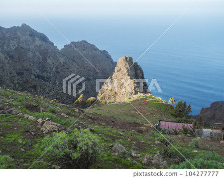 View of sharp rock formation and cliffs on top of La Merica mountain with palm trees, cacti and chicken hutch. Camino La Merica hiking trail. Arure, Valle Gran Rey , La Gomera, Canary Islands, Spain. View of sharp rock formation and cliffs on top of La Merica mountain with palm trees, cacti and chicken hutch. Camino La Merica hiking trail. Arure, Valle Gran Rey , La Gomera, Canary Islands, Spain. 104277777