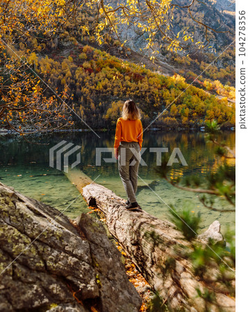 Woman at crystal lake in autumnal mountains. Mountain lake and traveller 104278356