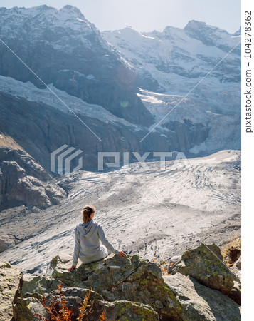 Hiker woman relaxing on stone near the mountains with glacier 104278362