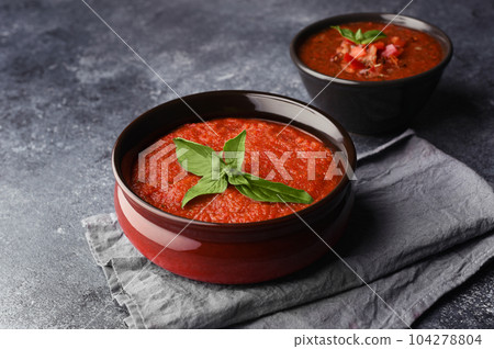 Two bowls with different types of homemade gazpacho. Traditional tomato cool soup with basil on and spicy gazpacho with pepper. Copy space. Red tomatoes soup ready to eat. Two bowls with different types of homemade gazpacho. Traditional tomato cool soup with basil on and spicy gazpacho with pepper. Copy space. Red tomatoes soup ready to eat. 104278804