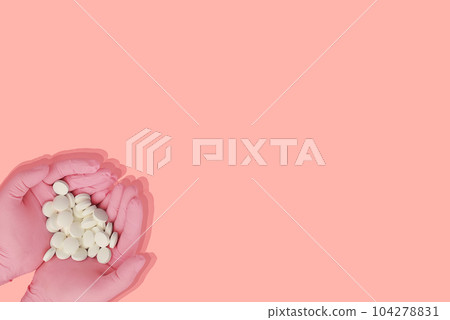Female hands in pink protective rubber medical gloves holdings white pills on a pink background. Vitamins in the hands. Copy space. Female hand holding a medicine, Woman hands with pills .  104278831
