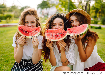 Cheerful happy friends camping on the grass, eating watermelon, laughing. 104279134