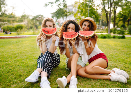Three young woman have fun together and eating watermelon in hot summer day. 104279135