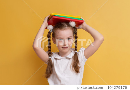 Cheerful schoolgirl holding books against a yellow wall background. The concept of education and school. Space for copying. High quality photo 104279176