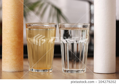 House water filtration system to drinkable condition. New clean water filter cartridge and glass of clear water. Used cartridge in rust and glass of dirty water on tabletop kitchen. World water day. 104279202