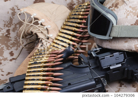 US MARINES. Machine gun with ammunition belt and armor helmet with protective goggles on uniform background. US MARINES. Machine gun with ammunition belt and armor helmet with protective goggles on uniform background. 104279306