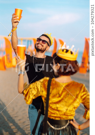 Lovely couple having fun at festival. Young friends with beer at beach party. Summer holiday, vacation. Lovely couple having fun at festival. Young friends with beer at beach party. Summer holiday, vacation. 104279321