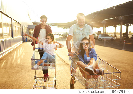 Group of happy young people having fun on shopping trolleys. Multiethnic young people racing on shopping cart. Group of happy young people having fun on shopping trolleys. Multiethnic young people racing on shopping cart. 104279364