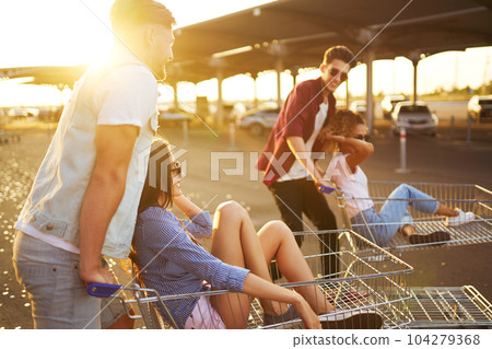 Group of happy young people having fun on shopping trolleys. Multiethnic young people racing on shopping cart. Group of happy young people having fun on shopping trolleys. Multiethnic young people racing on shopping cart. 104279368