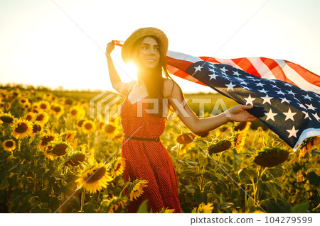 Beautiful girl in hat with the American flag in a sunflower field. 4th of July. Fourth of July. Independence Day. 104279599