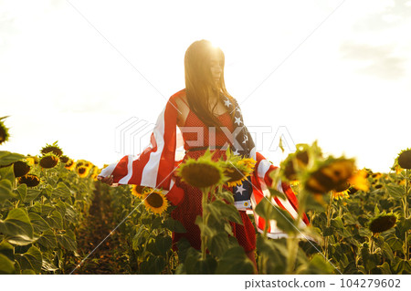 Beautiful girl in hat with the American flag in a sunflower field. 4th of July. Fourth of July. Freedom 104279602