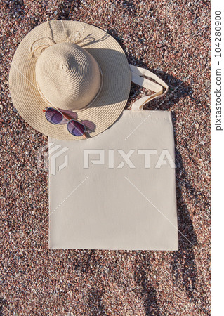 Summer beach accessories linen eco bag, straw hat and sunglasses on pebble beach near the sea. Summer beach accessories linen eco bag, straw hat and sunglasses on pebble beach near the sea. 104280900