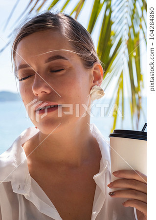 Woman hold takeaway coffee cup walking by seashore. Summery female portrait. 104284860